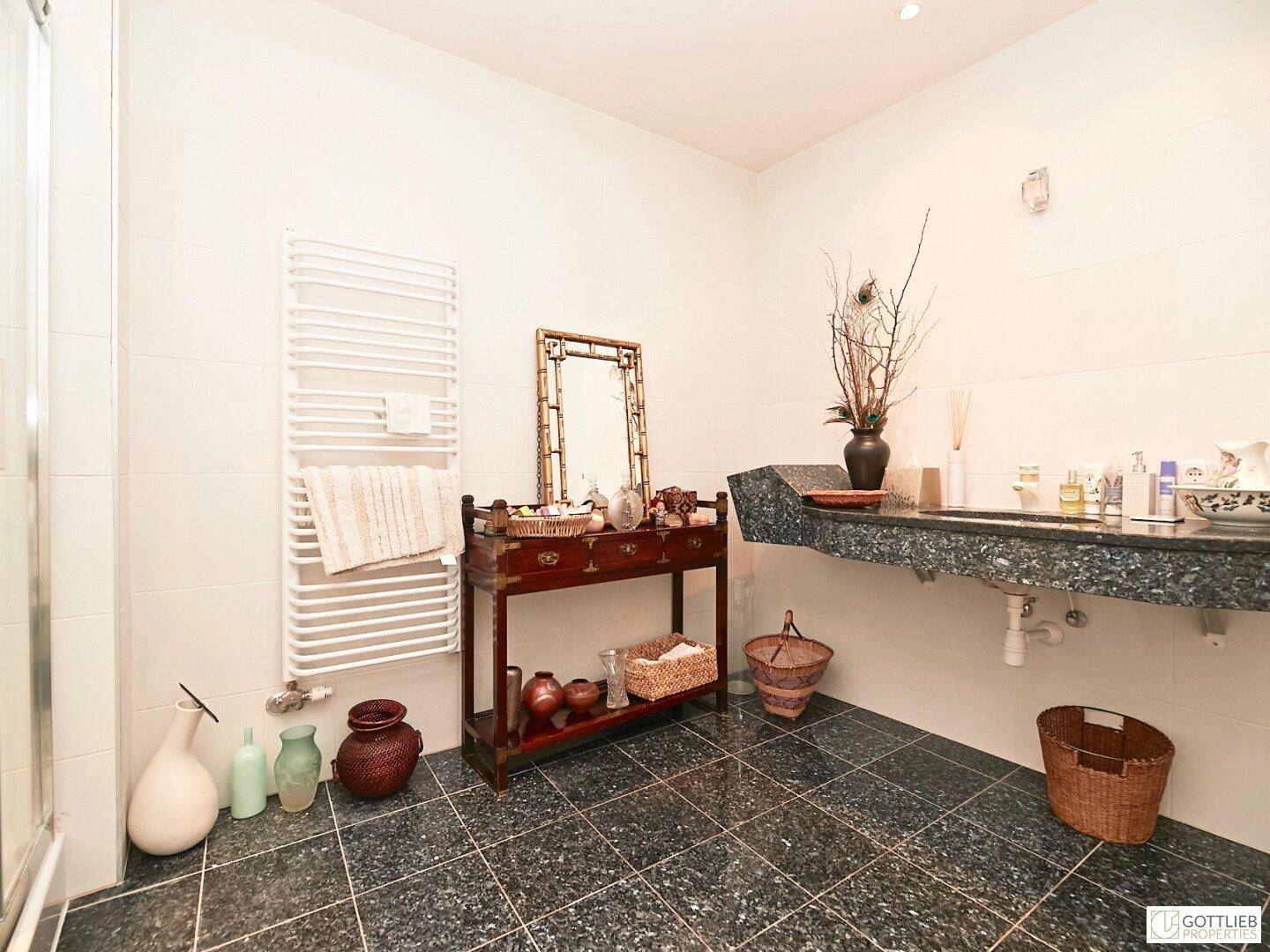 Modernes Badezimmer mit dunklen Granitfliesen, Einzelwaschbecken und Handtuchheizkörper.