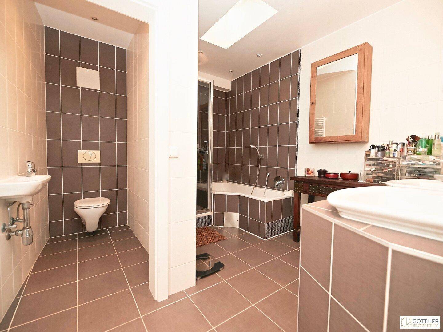 Badezimmer mit braunen und beigen Fliesen, Badewanne, Dusche und Oberlicht.