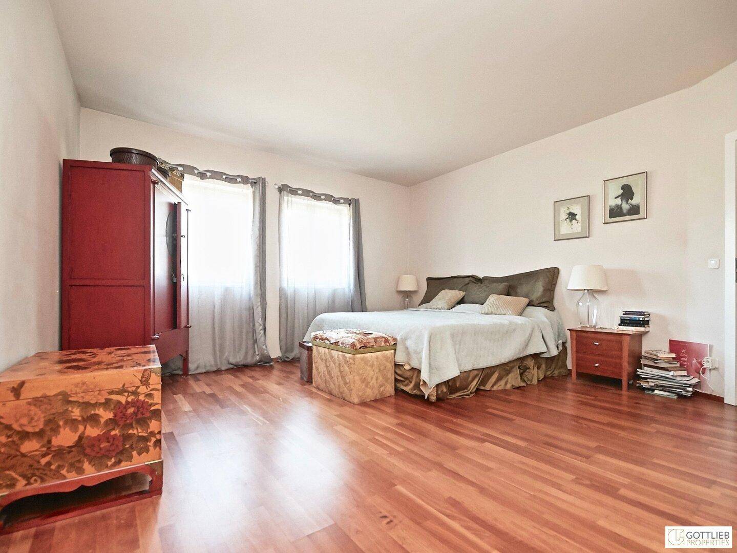 Helles Schlafzimmer mit Holzboden, großem Bett und zwei Fenstern für viel Licht.