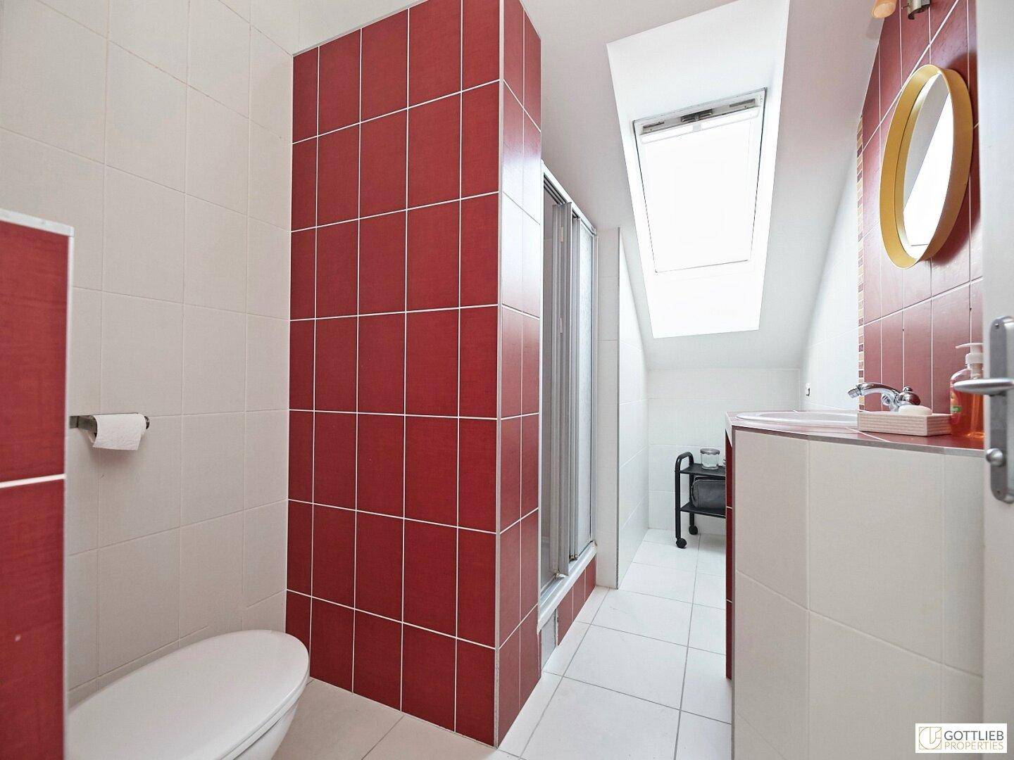 Modernes Badezimmer im Dachgeschoss mit roten und weißen Fliesen, Dusche und Dachfenster.