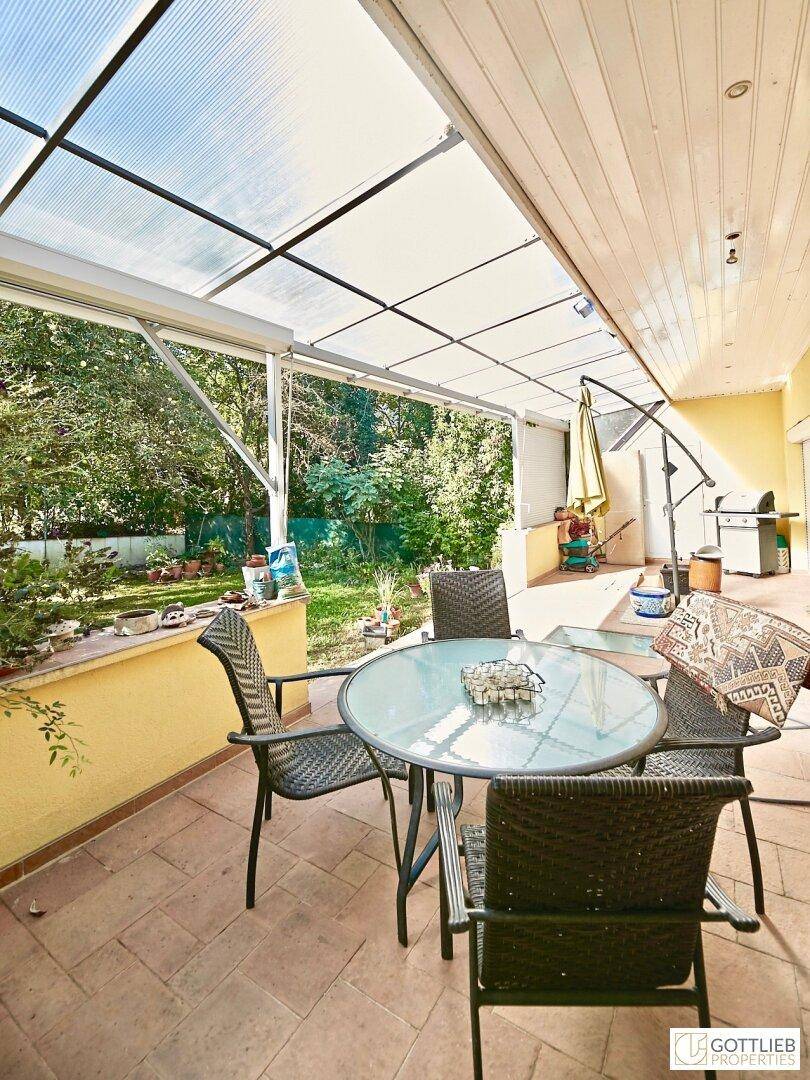 Überdachte Terrasse mit Gartenmöbeln, Fliesenboden und Blick ins Grüne.