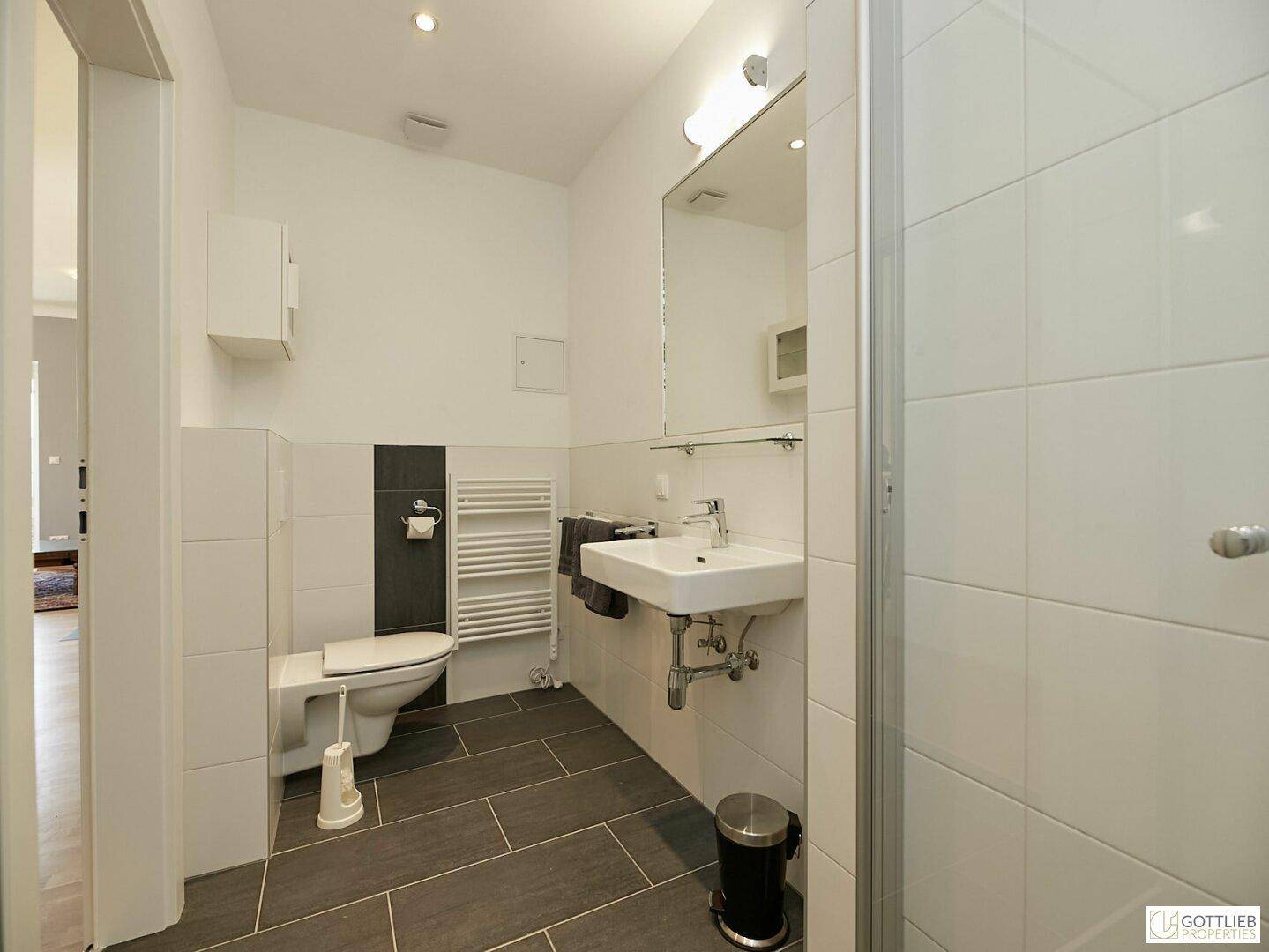 Funktionales Badezimmer mit WC, Waschbecken und Duschkabine in hellen Farbtönen.