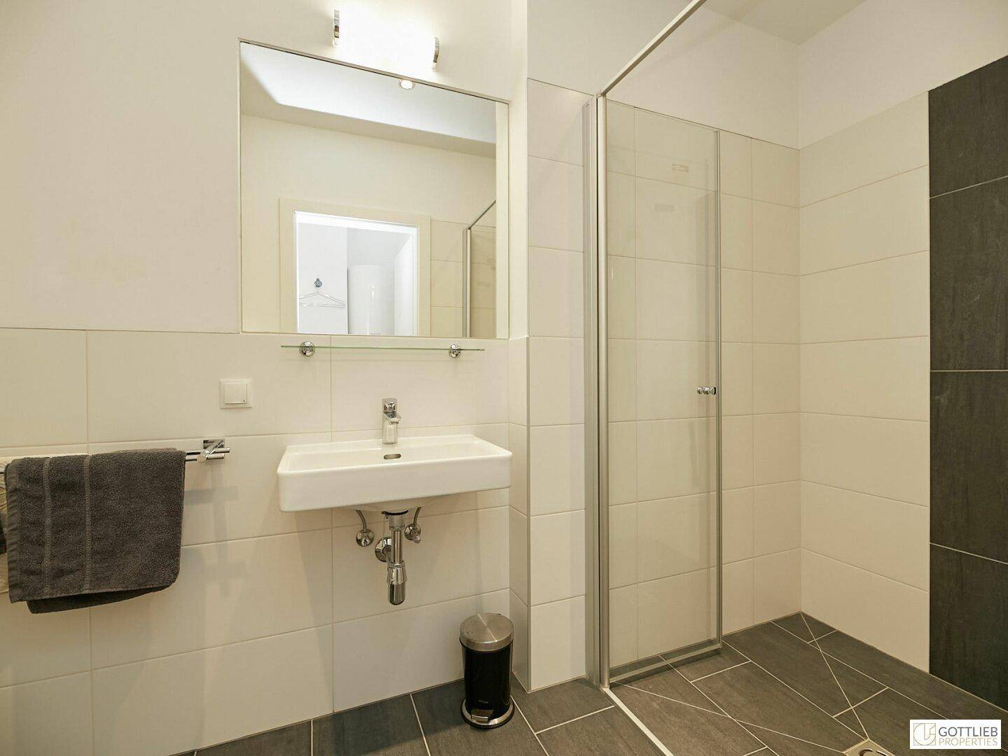 Modernes Badezimmer mit ebenerdiger Dusche, Waschbecken und dunklen Bodenfliesen.