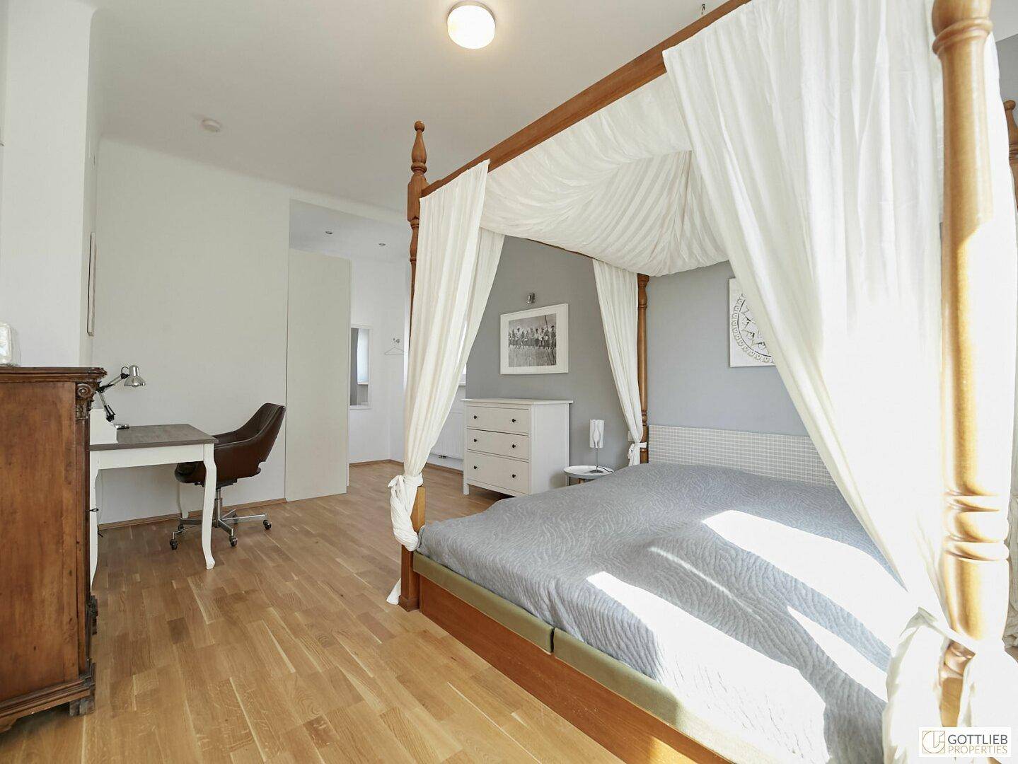 Schlafzimmer mit Holzboden, Himmelbett und Blick auf den integrierten Arbeitsplatz.