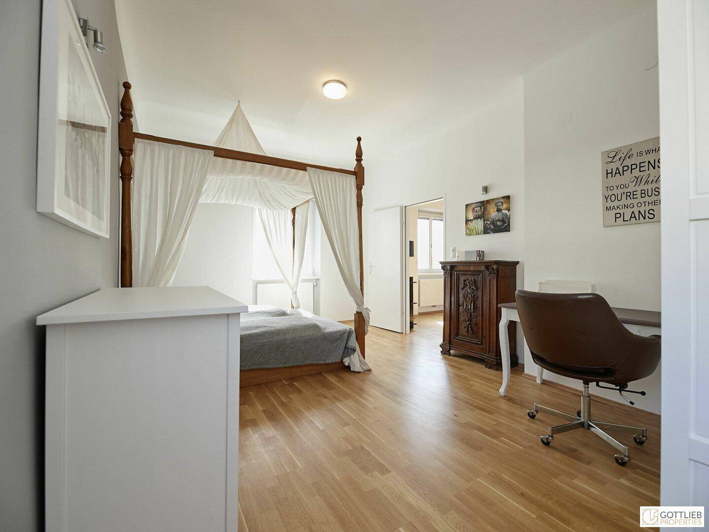 Geräumiges Schlafzimmer mit Holzboden, Himmelbett und integriertem Arbeitsbereich.