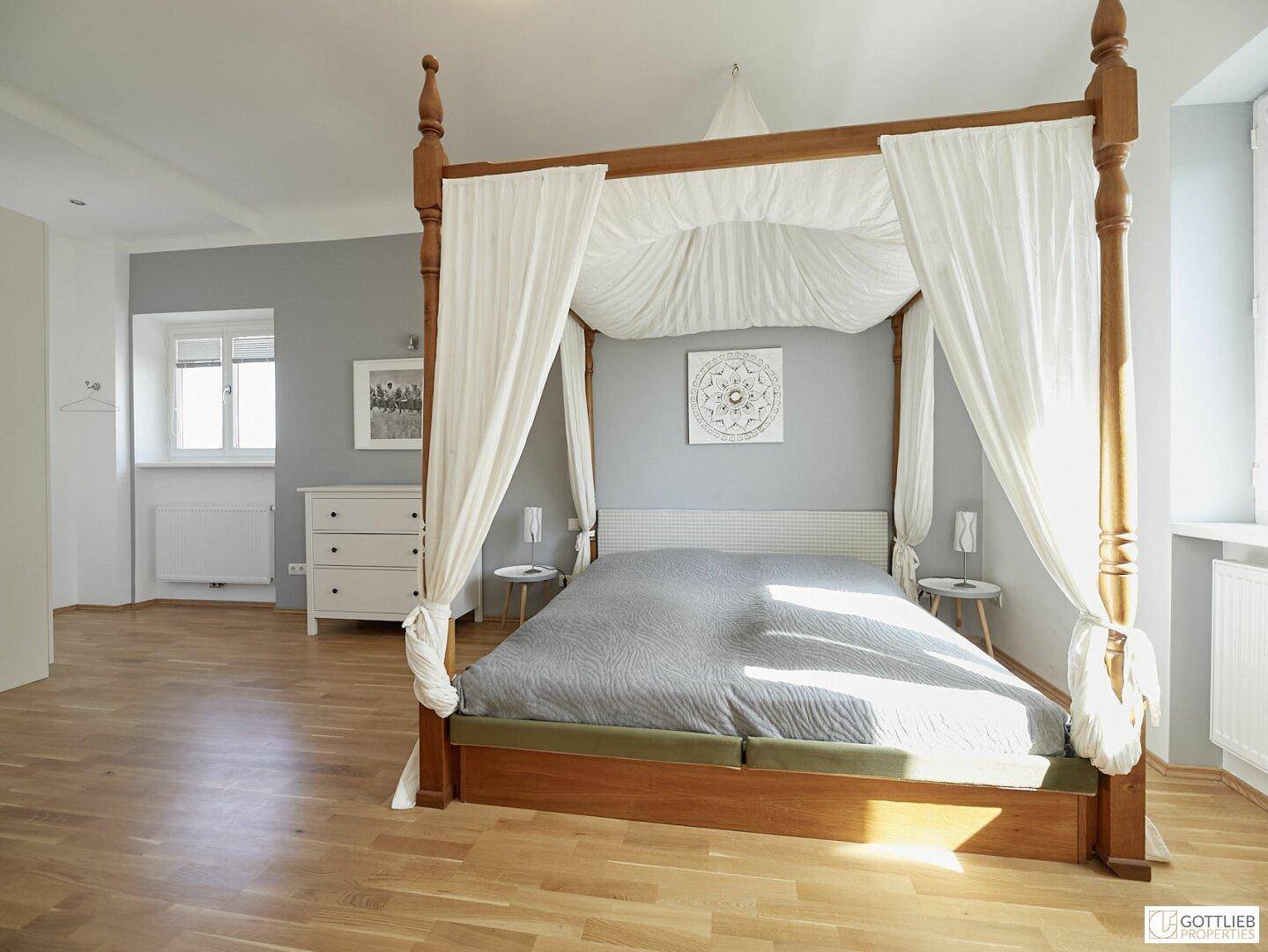 Helles Schlafzimmer mit Holzboden, Himmelbett und dezenter Wandgestaltung.