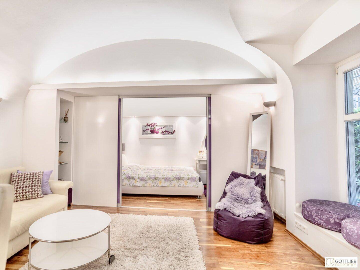 Wohnbereich mit Holzboden und Schiebetür, die zu einem Schlafzimmer führt.