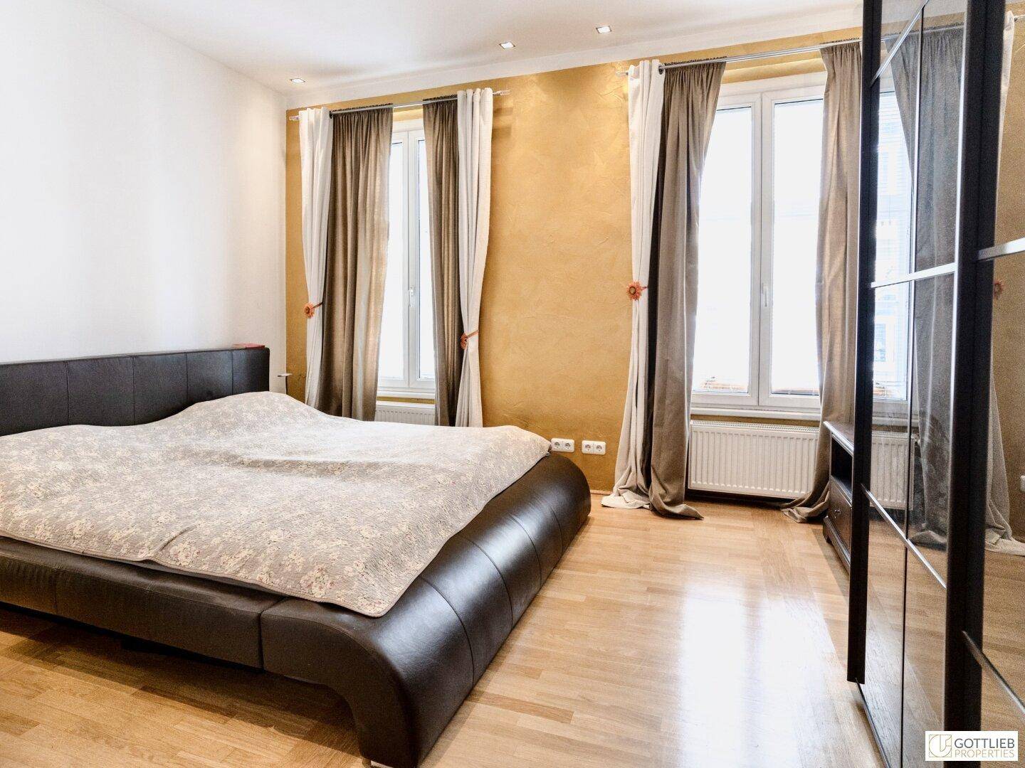 Geräumiges Schlafzimmer mit großem Doppelbett, Holzboden und zwei Fenstern mit Vorhängen.