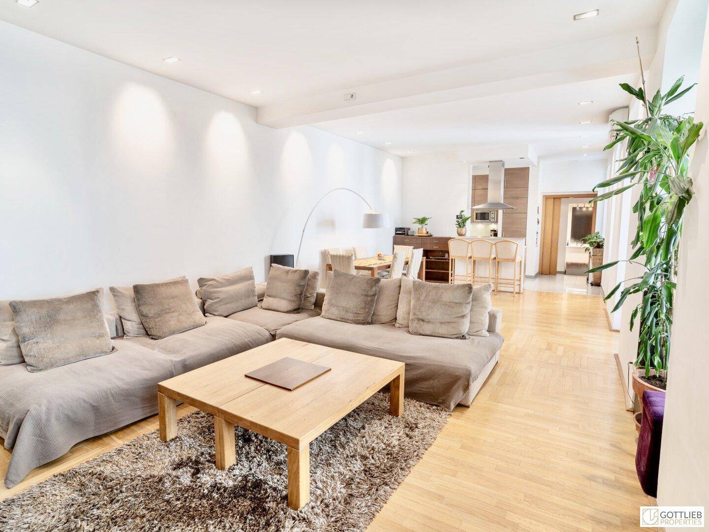 Geräumiger offener Wohn- und Essbereich mit beigem Sofa, Holzboden und Blick zur Küche.