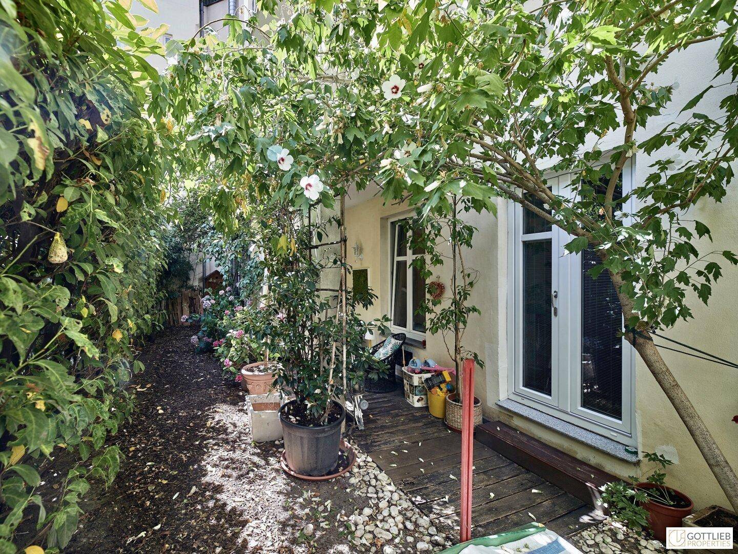 Grüner Gartenbereich mit Holzterrasse und üppiger Bepflanzung.