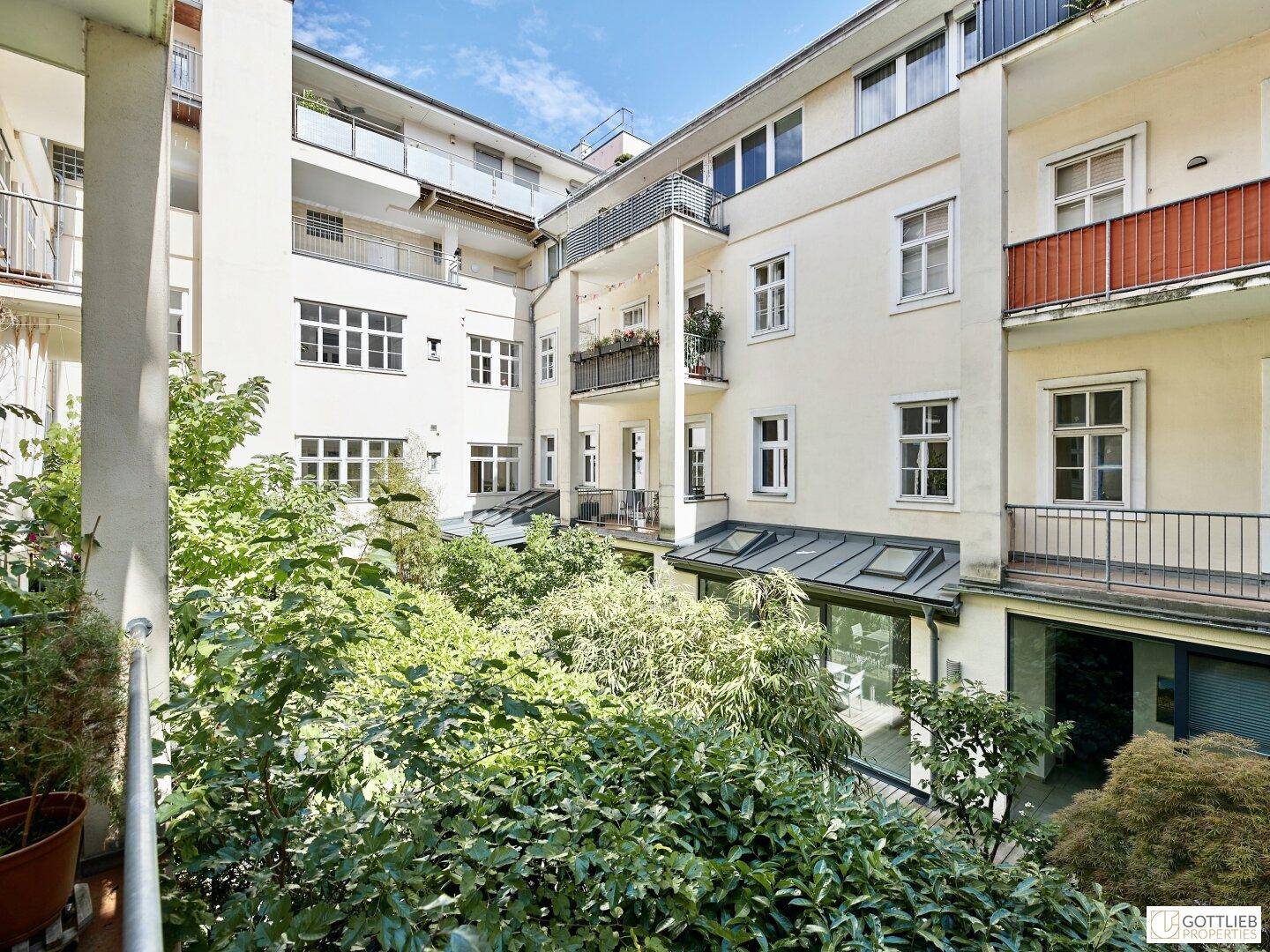 Grüner Innenhof mit üppiger Vegetation und mehreren Balkonen an den umliegenden Gebäuden.