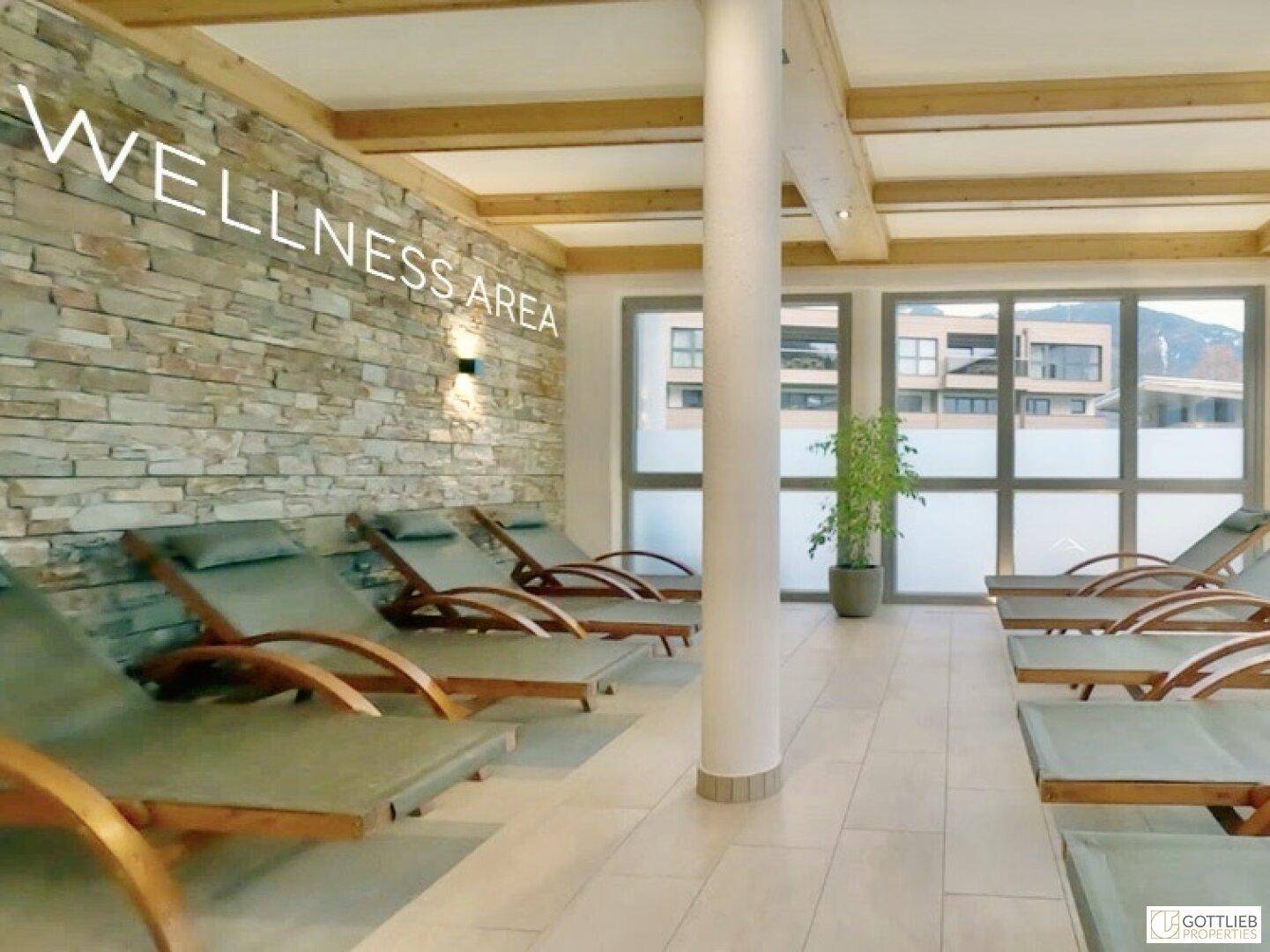 Entspannungsbereich mit bequemen Liegen, Steinwand und großen Fenstern in einem Wellnessbereich.
