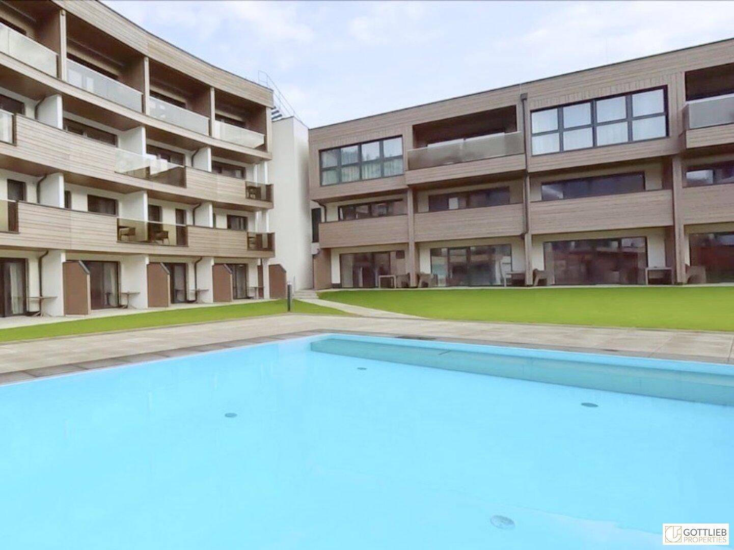 Moderner Gebäudekomplex mit Außenpool und gepflegter Rasenfläche, umgeben von zeitgenössischer Architektur.