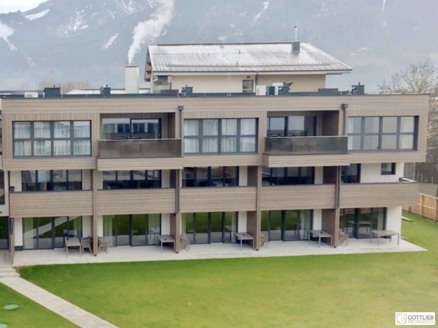 Moderne Apartmentgebäude mit Balkonen und Terrassen, umgeben von Rasenflächen und Bergen.