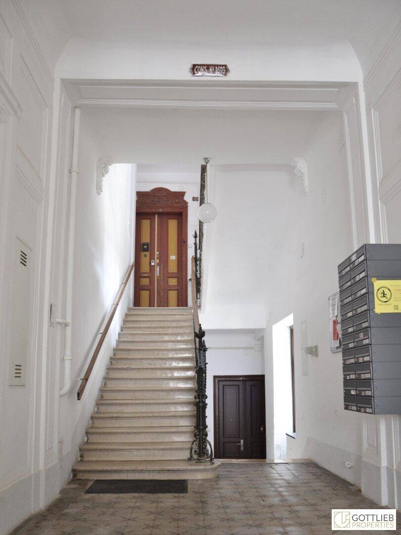 Großzügiges Treppenhaus mit Marmorstufen, schmiedeeisernem Geländer und Briefkästen im Eingangsbereich.