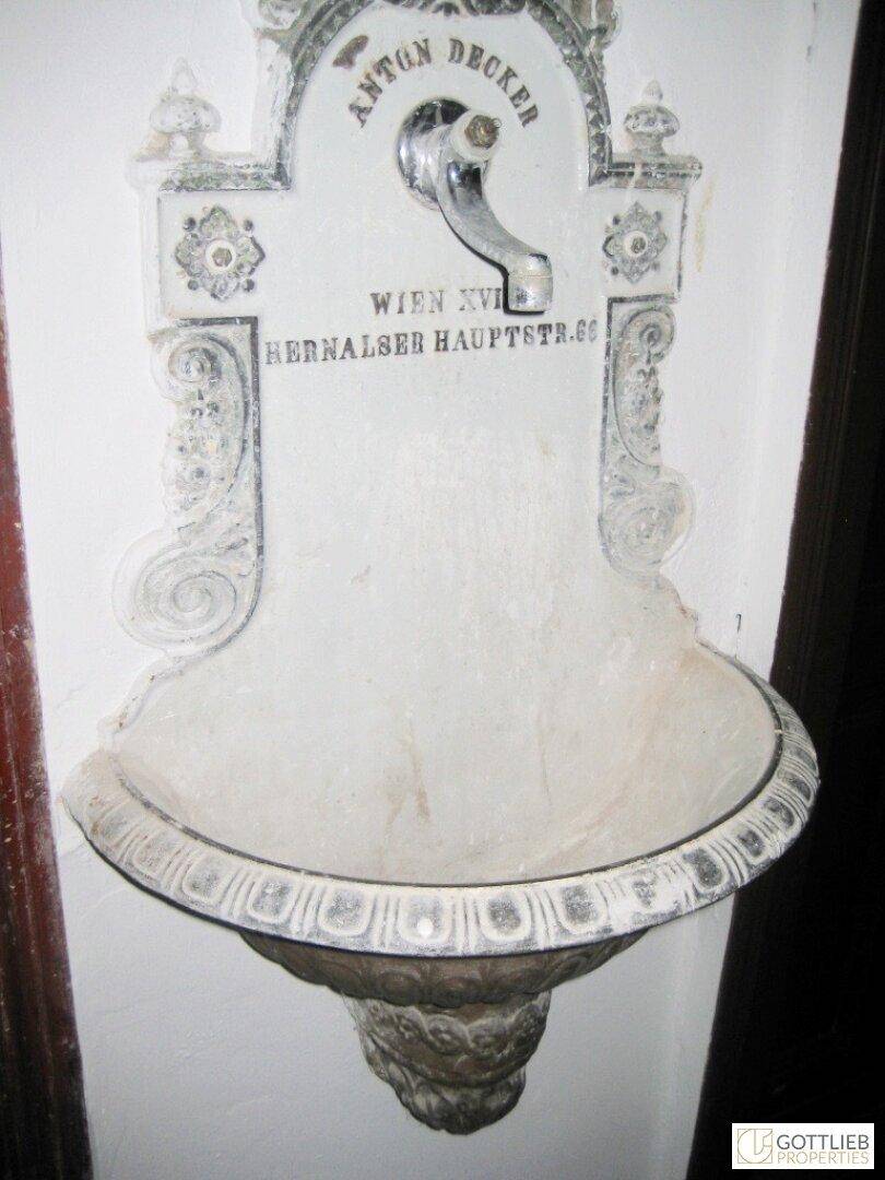 Historisches, verziertes Wandwaschbecken mit Inschrift, möglicherweise in einem Flur oder Treppenhaus.