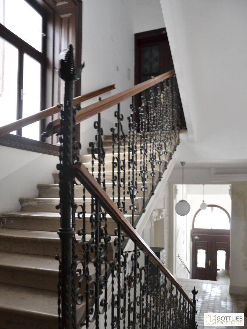 Elegantes Treppenhaus mit schmiedeeisernem Geländer und Holzhandlauf in einem Altbau.