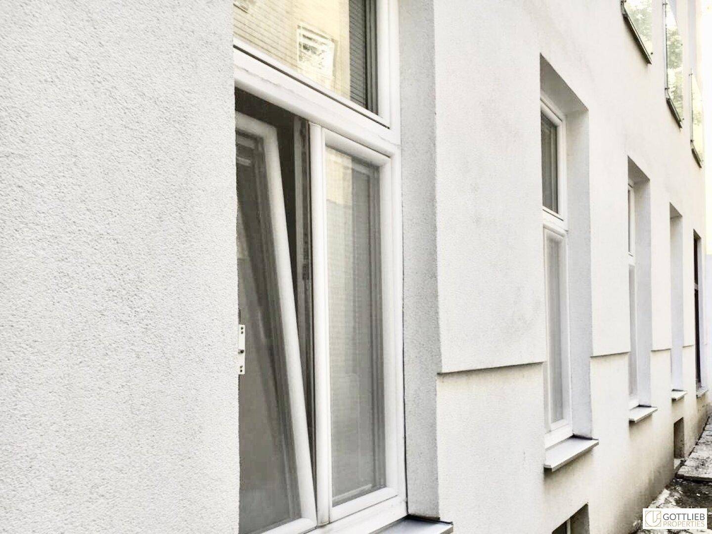 Weiße Gebäudefassade mit mehreren Fenstern, eines davon ist gekippt.