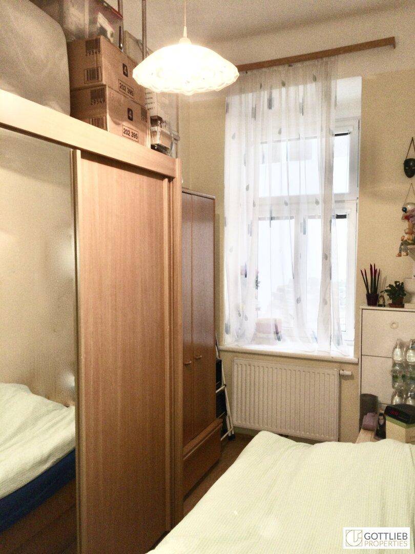 Schlafzimmer mit einem Bett, einem Holzschrank und einem Fenster mit hellen Vorhängen.