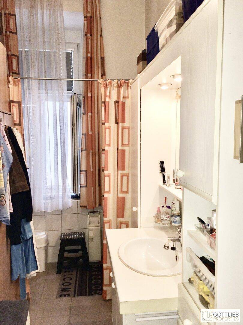 Kleines Badezimmer mit Waschbecken, Spiegel und Duschvorhang, ausgestattet mit Fliesenboden.