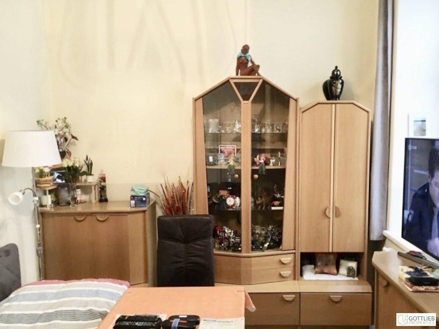 Gemütliches Wohnzimmer mit Holzmöbeln, einem Sofa und einem dekorativen Vitrinenschrank.