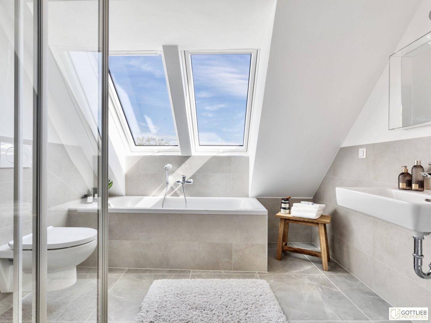 Modernes Badezimmer im Dachgeschoss mit Badewanne, Dusche, Waschbecken und Dachfenstern.