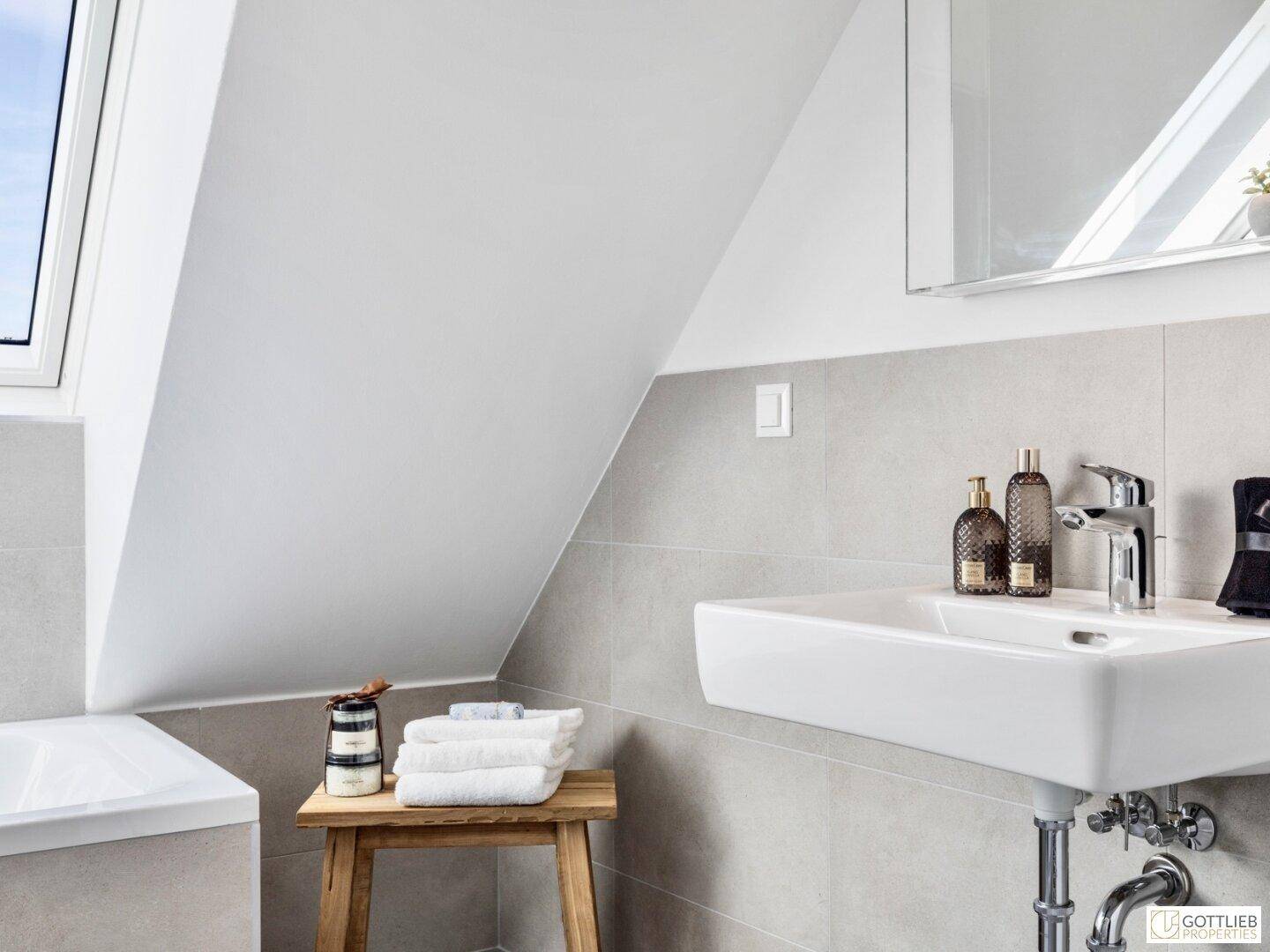 Detailansicht des modernen Badezimmers mit Waschbecken, Spiegel und grauen Fliesen.