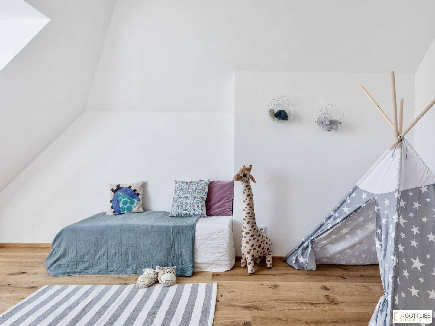 Kinderzimmer im Dachgeschoss mit Bett, Spielzelt, Giraffen-Stofftier und Holzboden.
