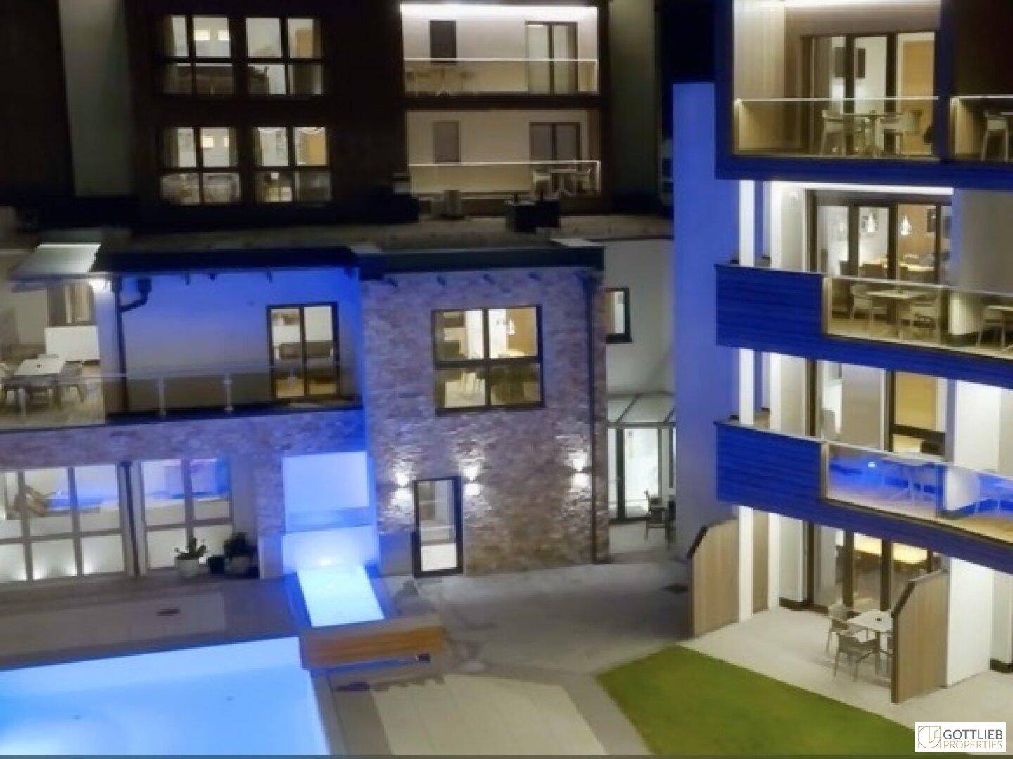 Moderne Apartmentanlage bei Nacht mit beleuchtetem Poolbereich und Terrassen.