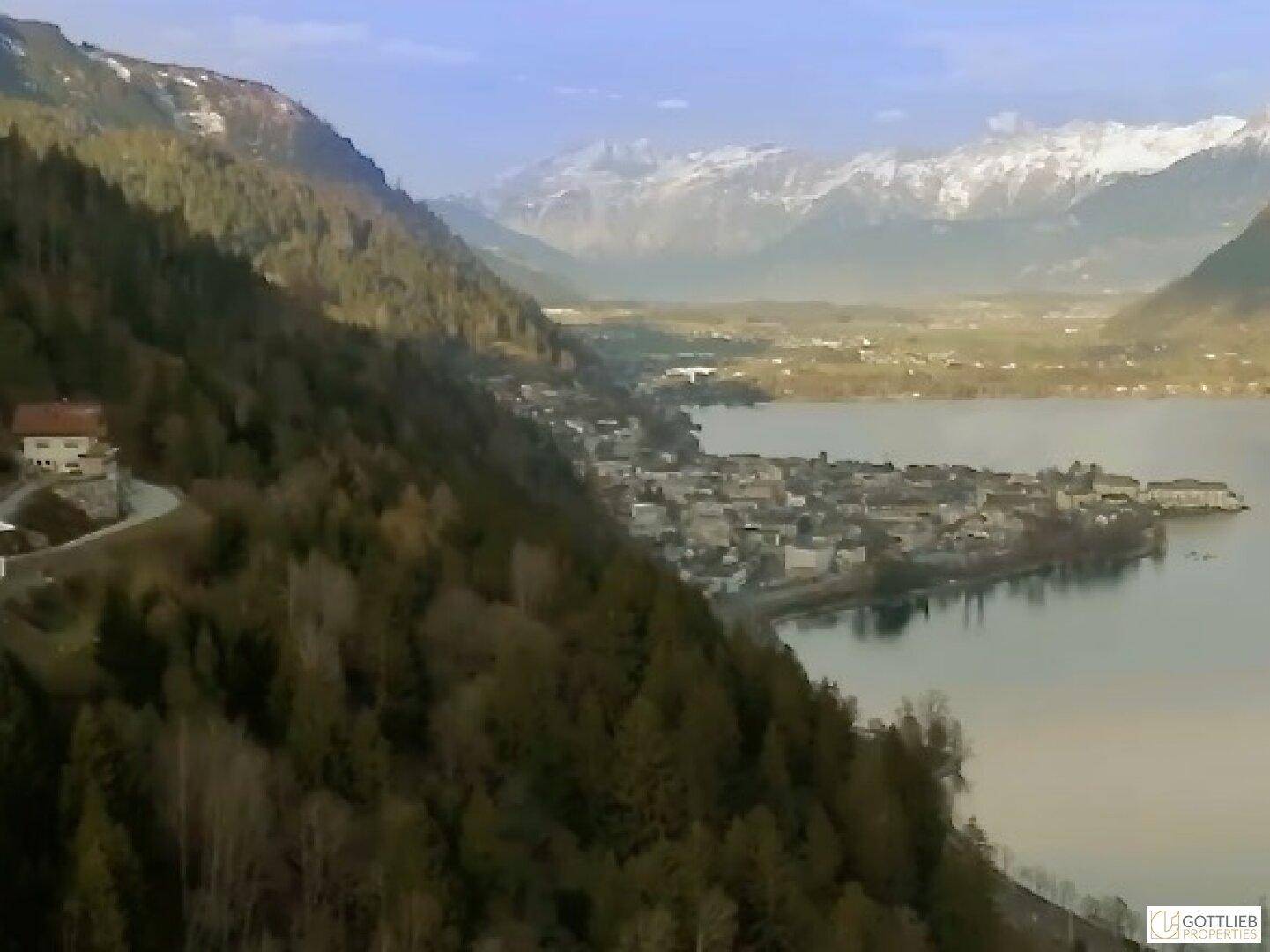 Weitläufige Luftaufnahme einer Stadt am See, eingebettet in eine beeindruckende Berg- und Waldlandschaft.