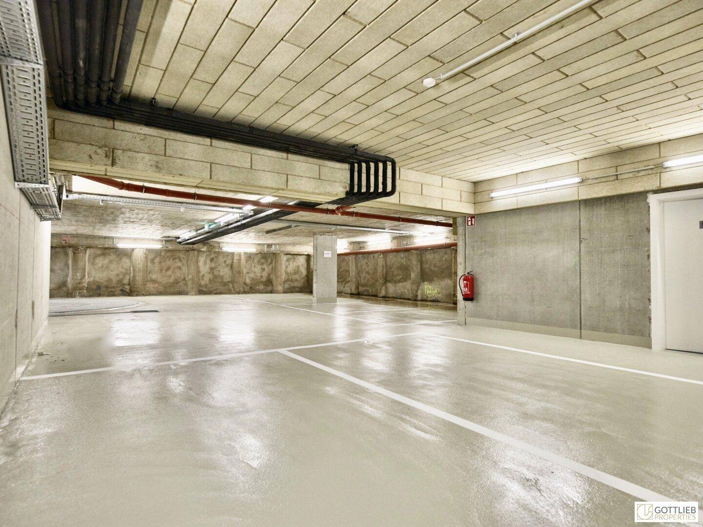 Geräumige Tiefgarage mit Betonwänden, markierten Stellplätzen und Brandschutzvorrichtung.