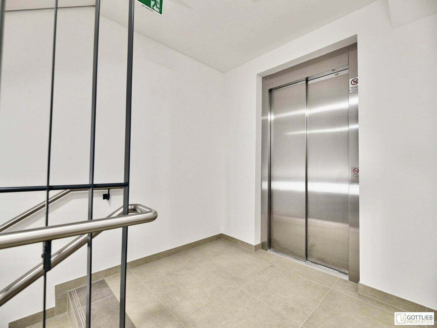 Moderner Eingangsbereich mit Aufzug und Treppenhaus in einem Mehrfamilienhaus.