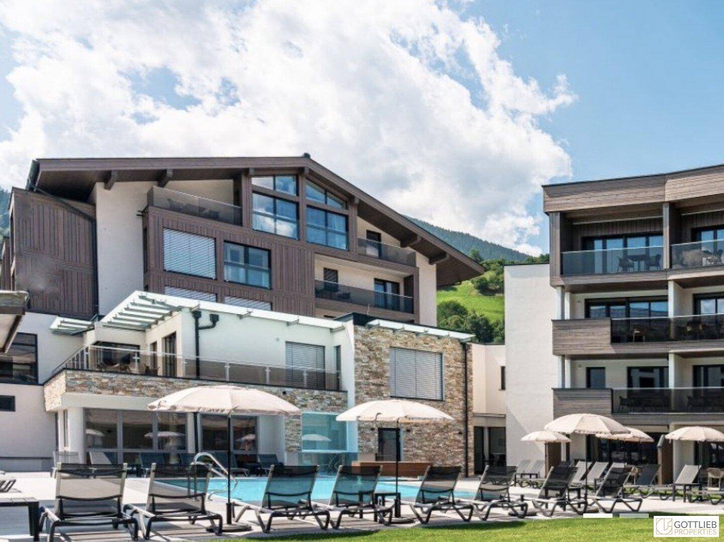 Außenbereich mit Pool, Liegestühlen und Sonnenschirmen, umgeben von moderner Architektur und Bergen.