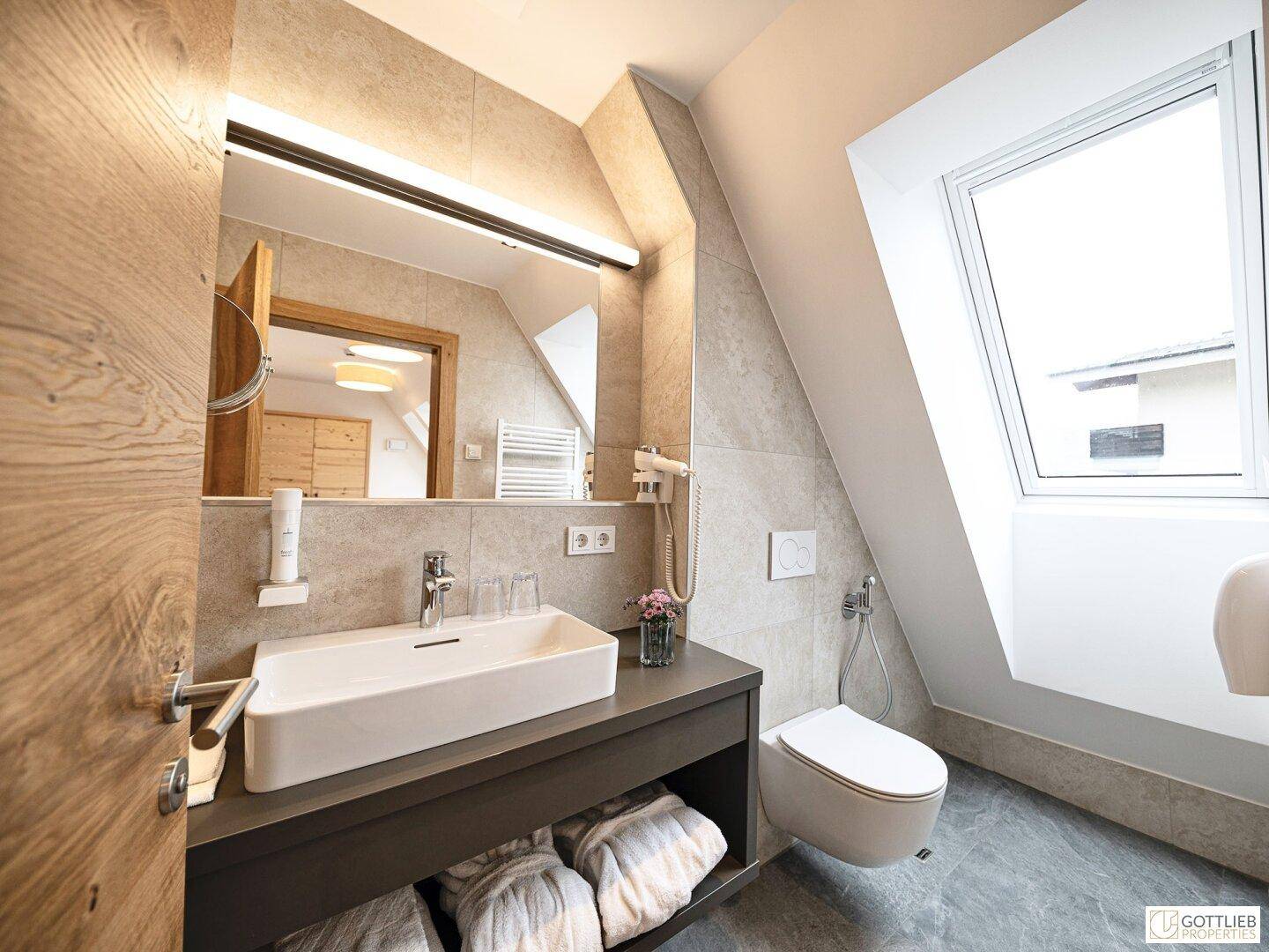 Modernes Badezimmer im Dachgeschoss mit Waschbecken, Toilette und Dachfenster.