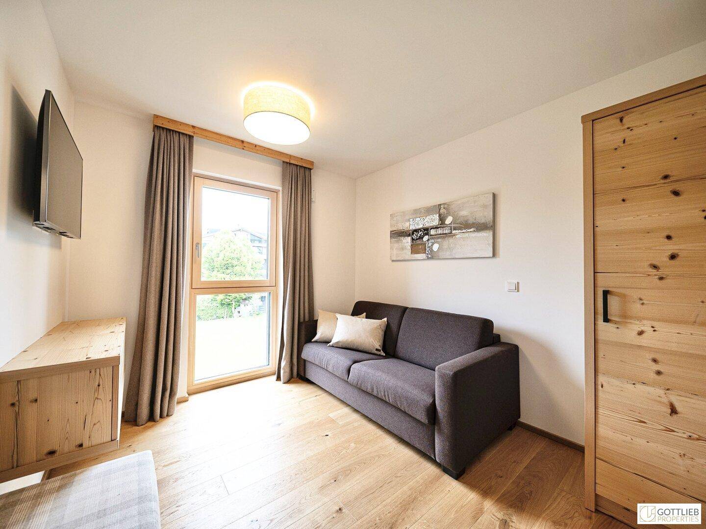 Kleines Schlafzimmer mit Holzboden, Schlafsofa und Fenster mit Blick ins Grüne.