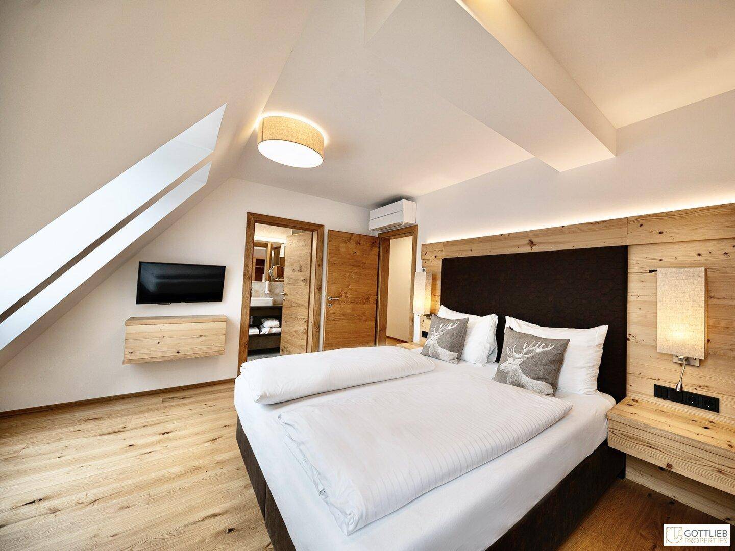 Modernes Schlafzimmer im Dachgeschoss mit Holzboden, Doppelbett und Zugang zum Badezimmer.