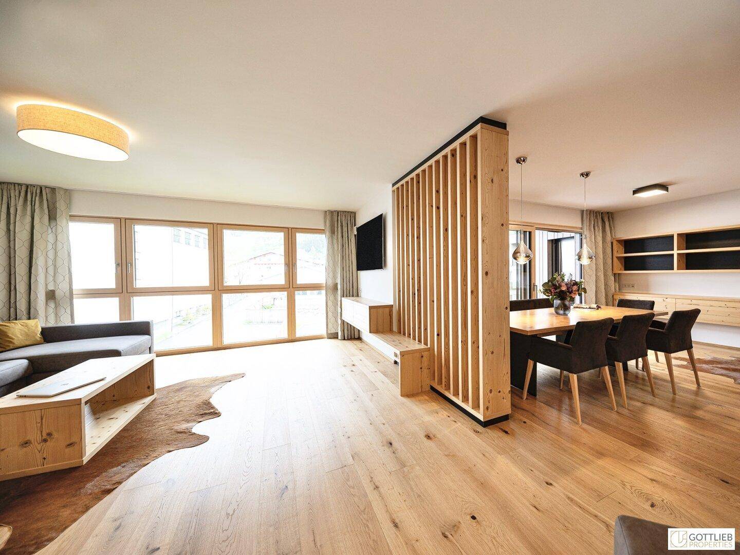 Heller Wohnbereich mit Holzboden, bequemer Couch und Essbereich, durch Holzlamellen getrennt.