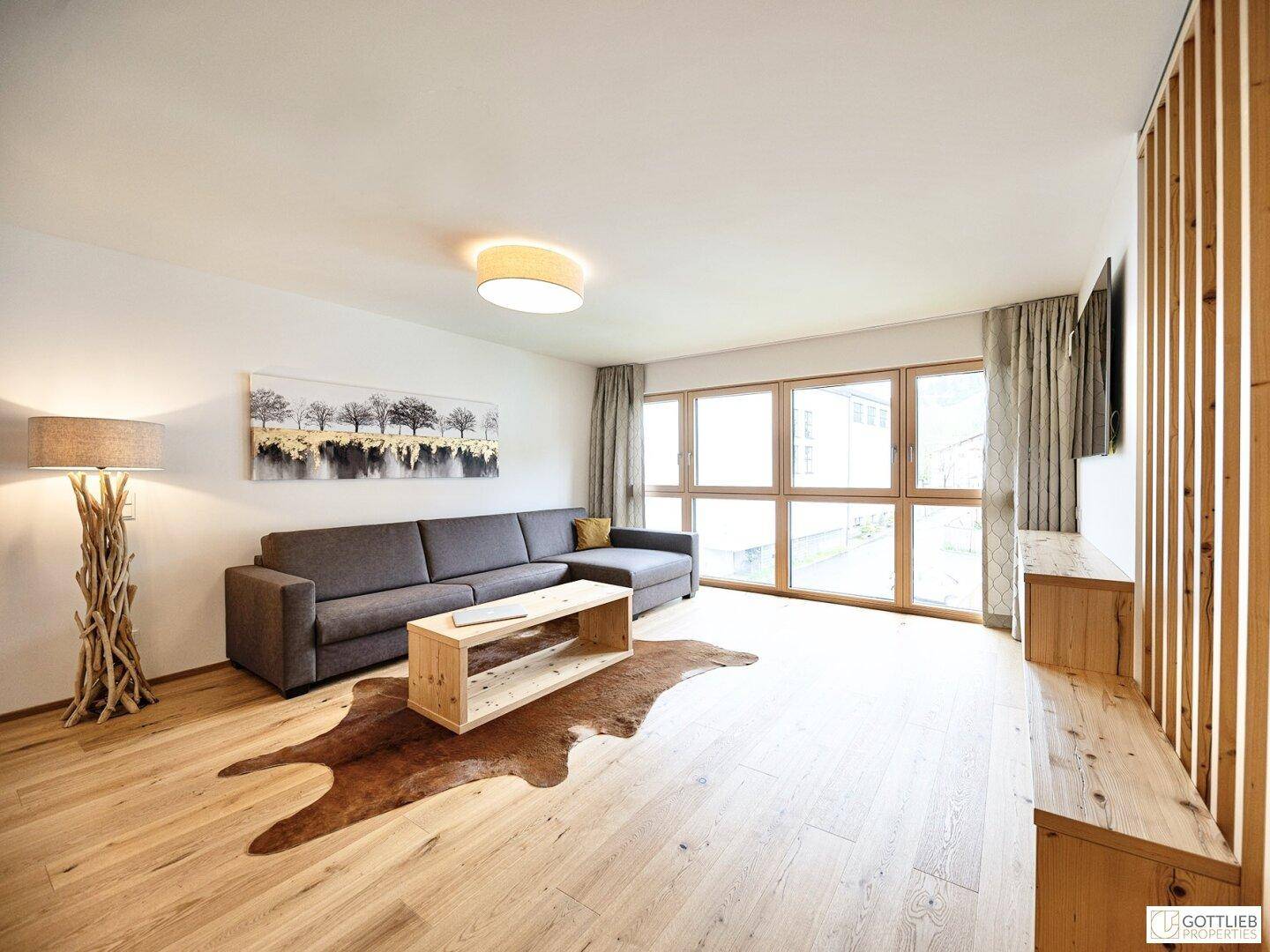Gemütliches Wohnzimmer mit großer Fensterfront, Holzboden und moderner Einrichtung.