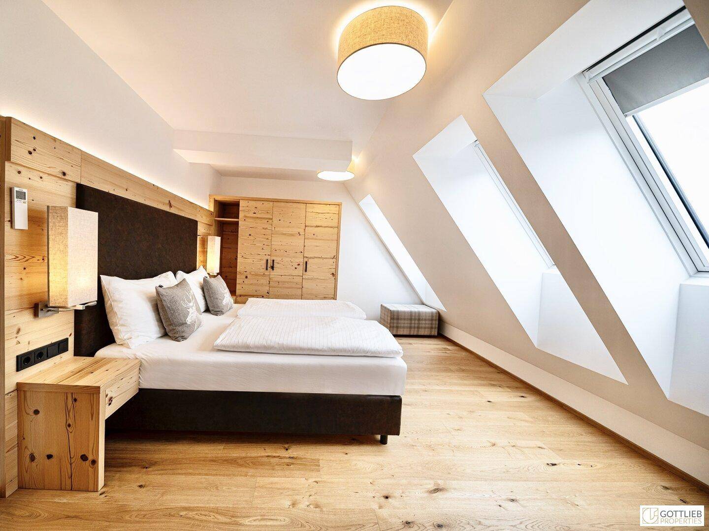 Modernes Schlafzimmer im Dachgeschoss mit Holzboden, Doppelbett und schrägen Dachfenstern.