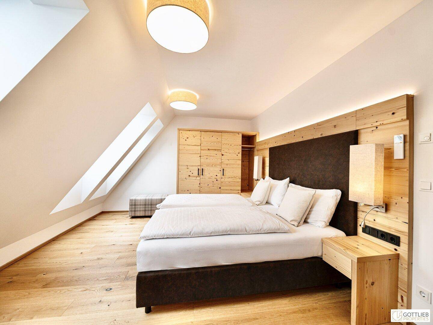 Helles Schlafzimmer im Dachgeschoss mit Holzboden, Doppelbett und Einbauschrank.