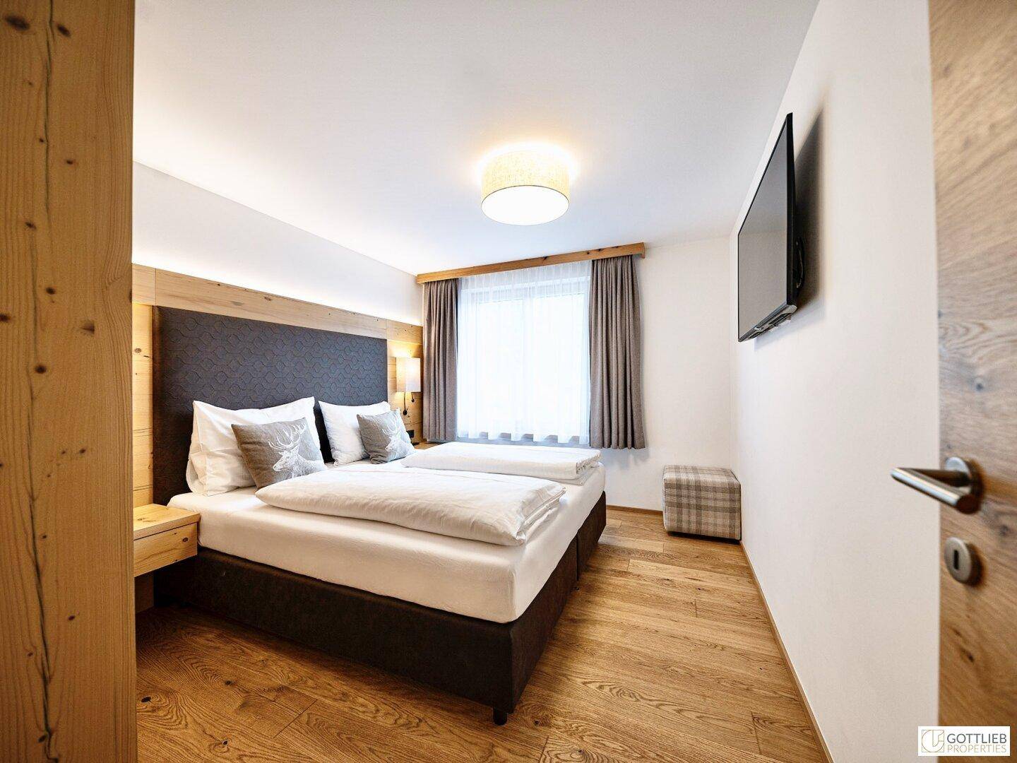 Komfortables Schlafzimmer mit Doppelbett, Holzboden und einem Fenster, das viel Tageslicht hereinlässt.