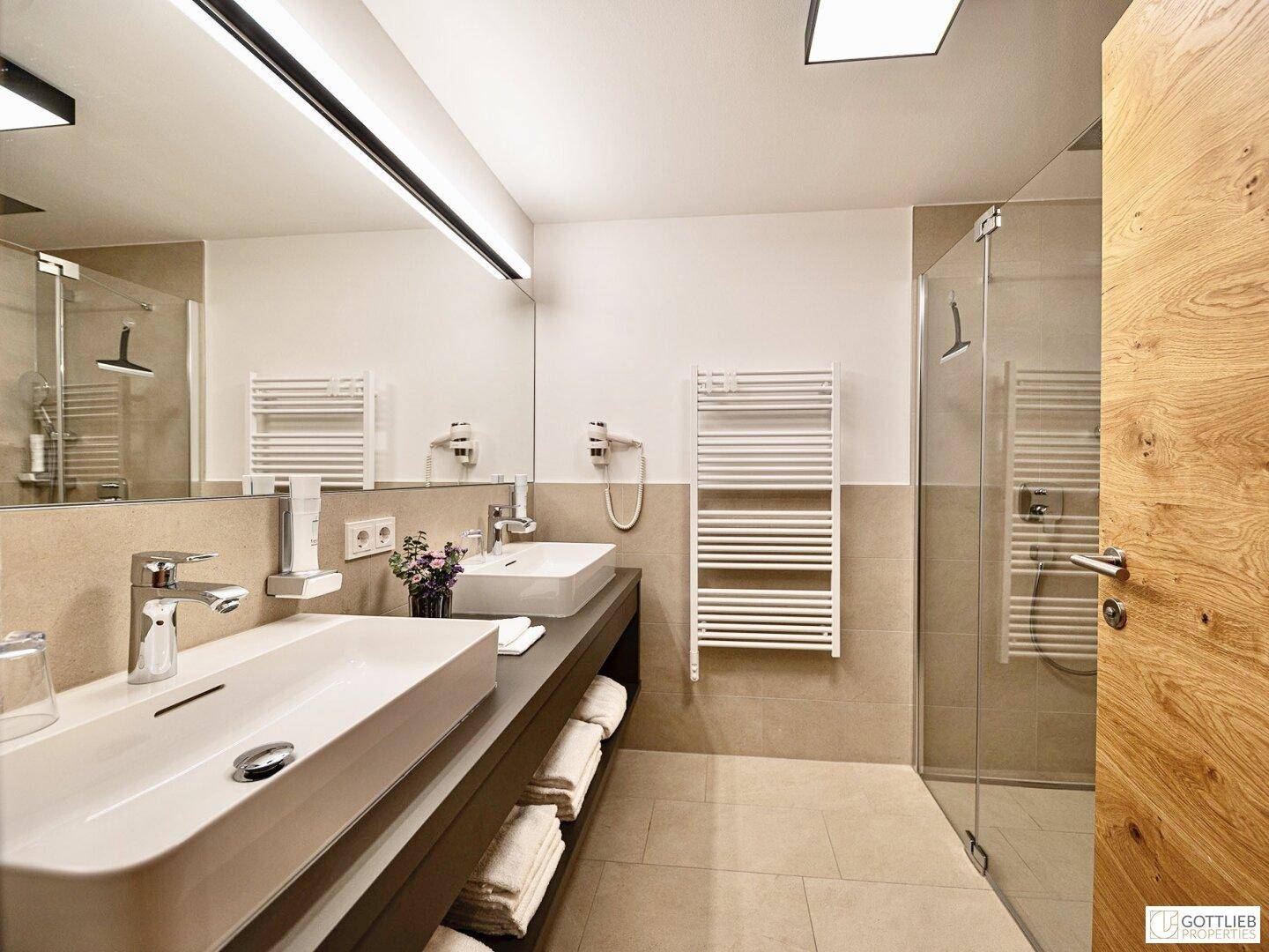 Stilvolles Badezimmer mit zwei Waschbecken, großem Spiegel und beheiztem Handtuchhalter.