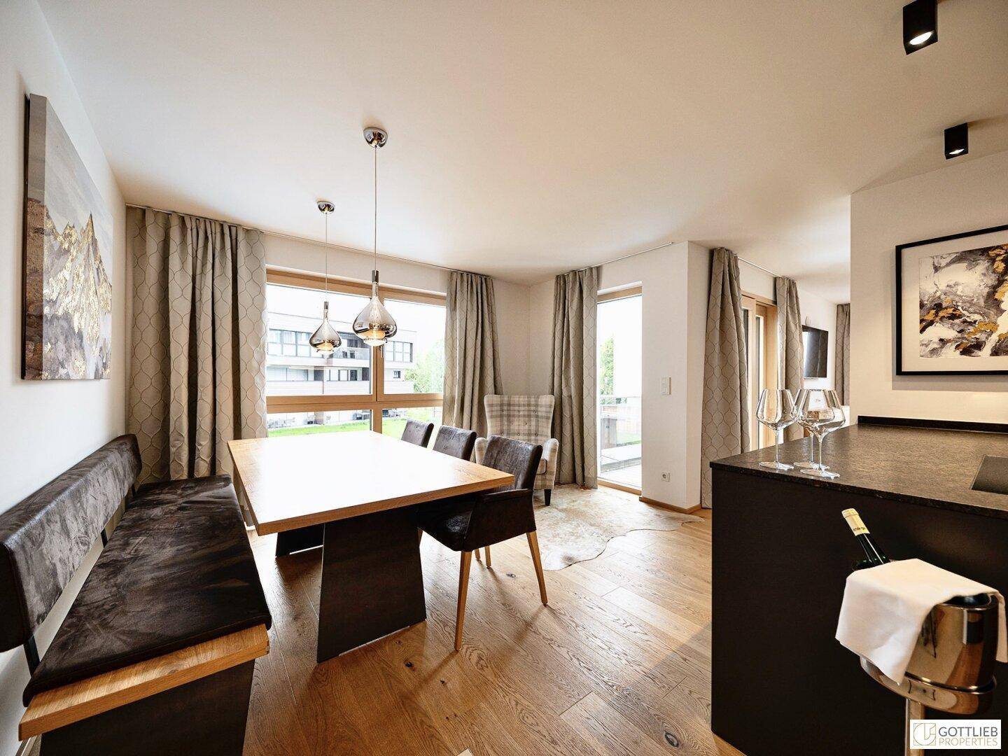 Gemütlicher Essbereich mit Holztisch und großen Fenstern, die viel Tageslicht hereinlassen.