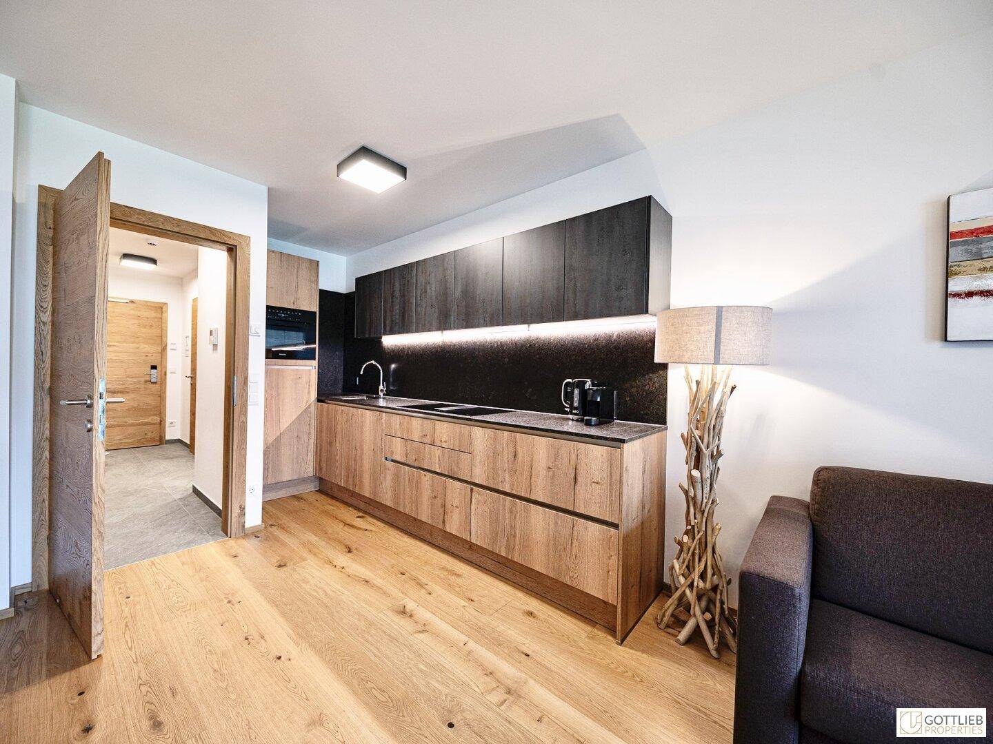 Kompakte, moderne Küche mit Holz- und dunklen Fronten, integrierten Geräten und Holzboden.