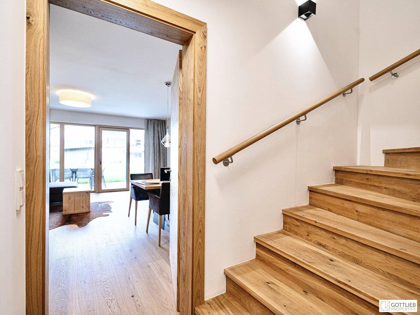 Heller Flur mit Holztreppe und Zugang zum offenen Wohnbereich.
