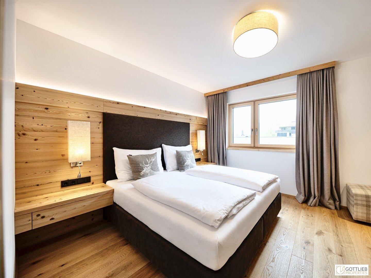 Helles Schlafzimmer mit Holzwand, Doppelbett und Fenster mit Blick nach draußen.