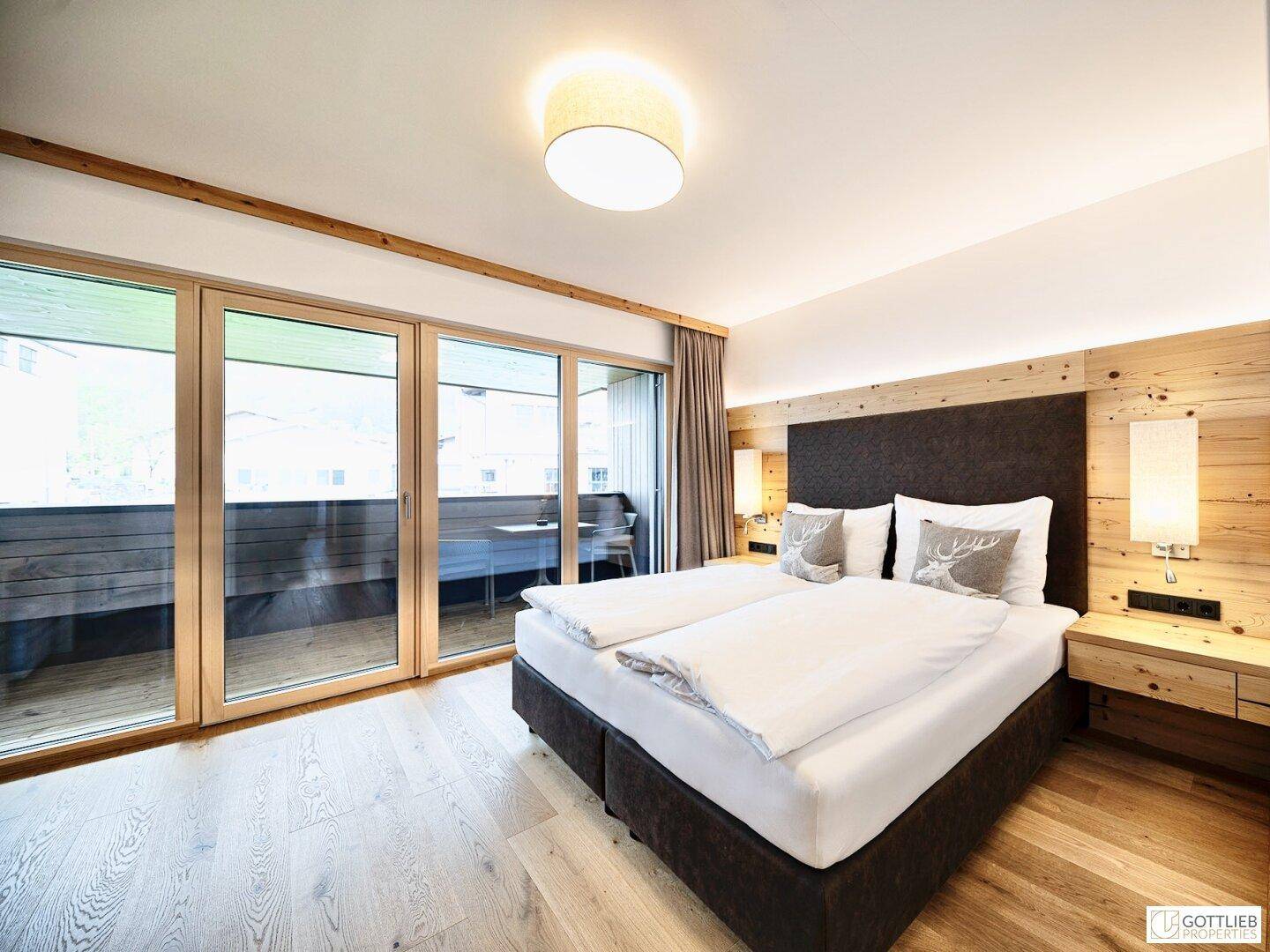 Gemütliches Schlafzimmer mit Holzwand, Doppelbett und Zugang zu einem Balkon.