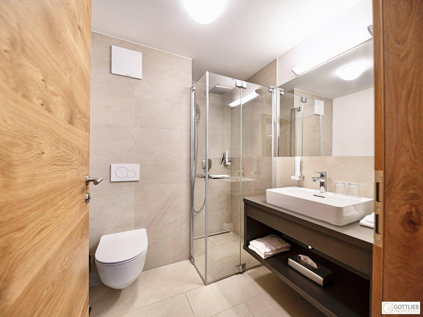 Zeitgemäßes Badezimmer mit Dusche, Wand-WC und Waschtisch, ausgestattet mit hellen Fliesen.