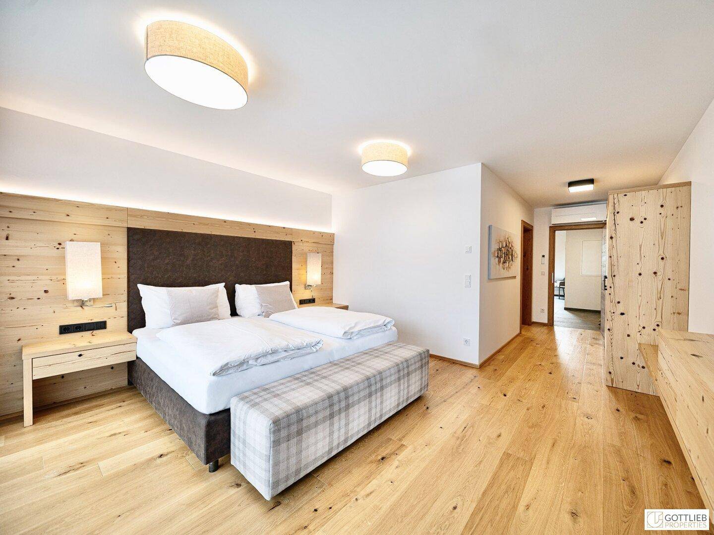 Helles Schlafzimmer mit Holzboden, Doppelbett und alpiner Holzwandgestaltung.