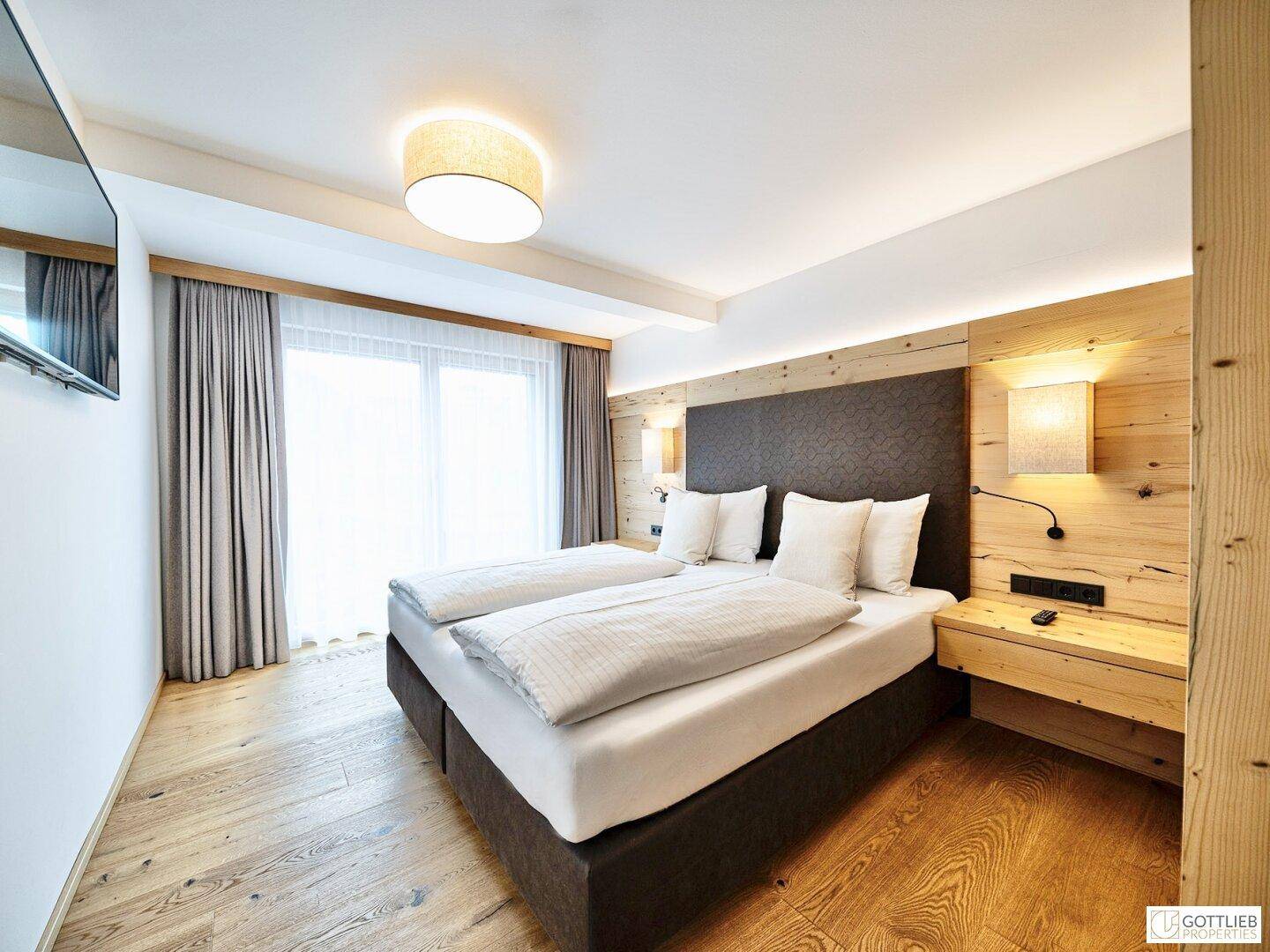 Helles Schlafzimmer mit Doppelbett, Holzwand und Flachbildfernseher, mit Holzboden und viel Licht.